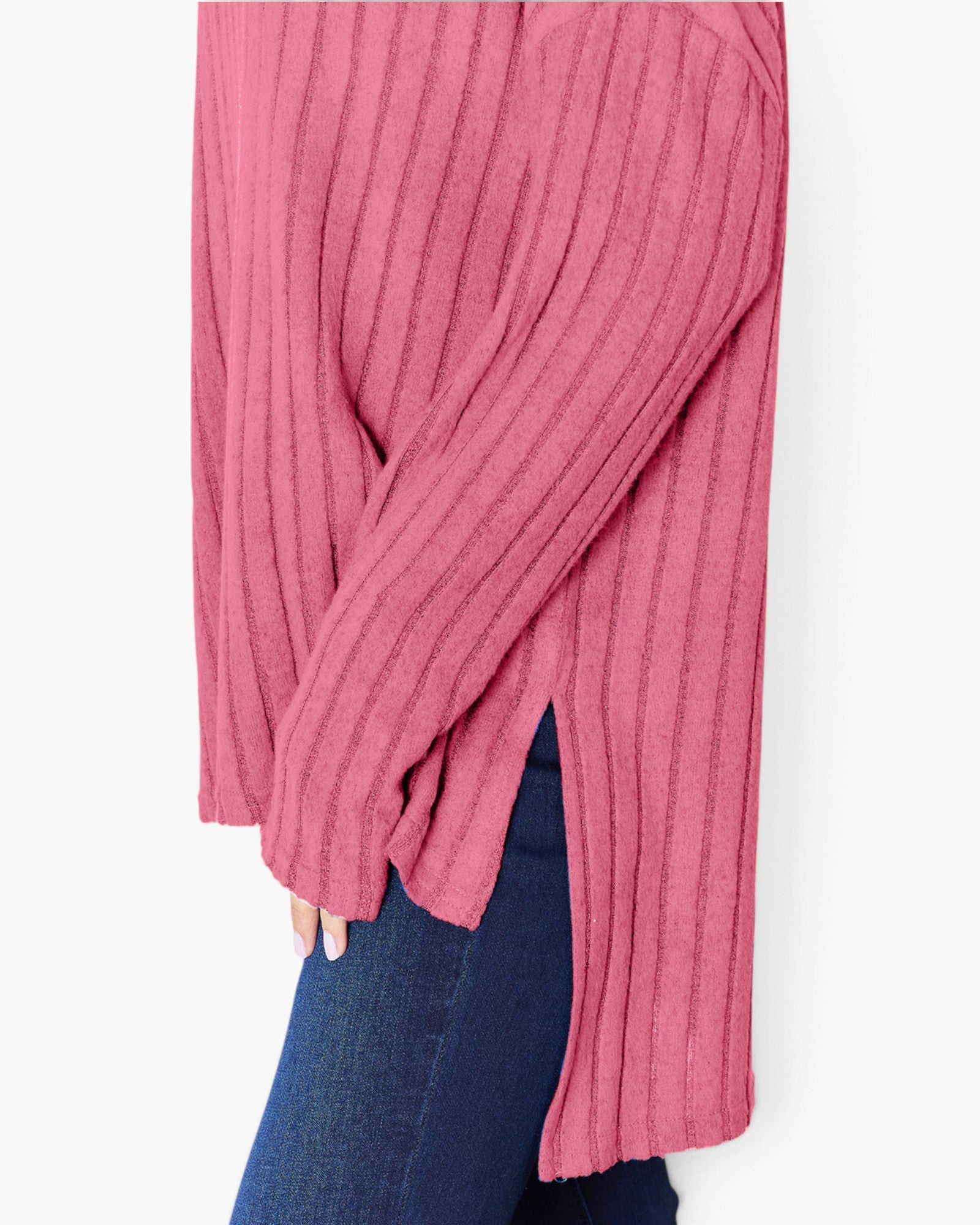 A close-up of a person wearing a ribbed knit long-sleeve top in dusty pink, paired with dark blue jeans against a plain light background.