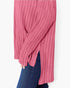 A close-up of a person wearing a ribbed knit long-sleeve top in dusty pink, paired with dark blue jeans against a plain light background.