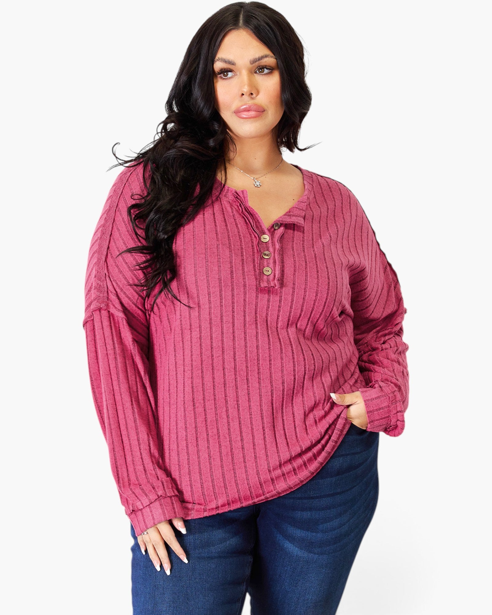 A woman modeling a long-sleeve ribbed henley top in a dusty rose pink color, paired with dark blue jeans, against a plain white background.