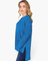 A woman modeling a bright blue ribbed knit long-sleeve top, shown from a side profile against a clean white studio background.