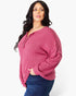 A woman modeling a ribbed long-sleeve henley top in dusty rose pink with blue jeans, photographed against a clean white studio background.