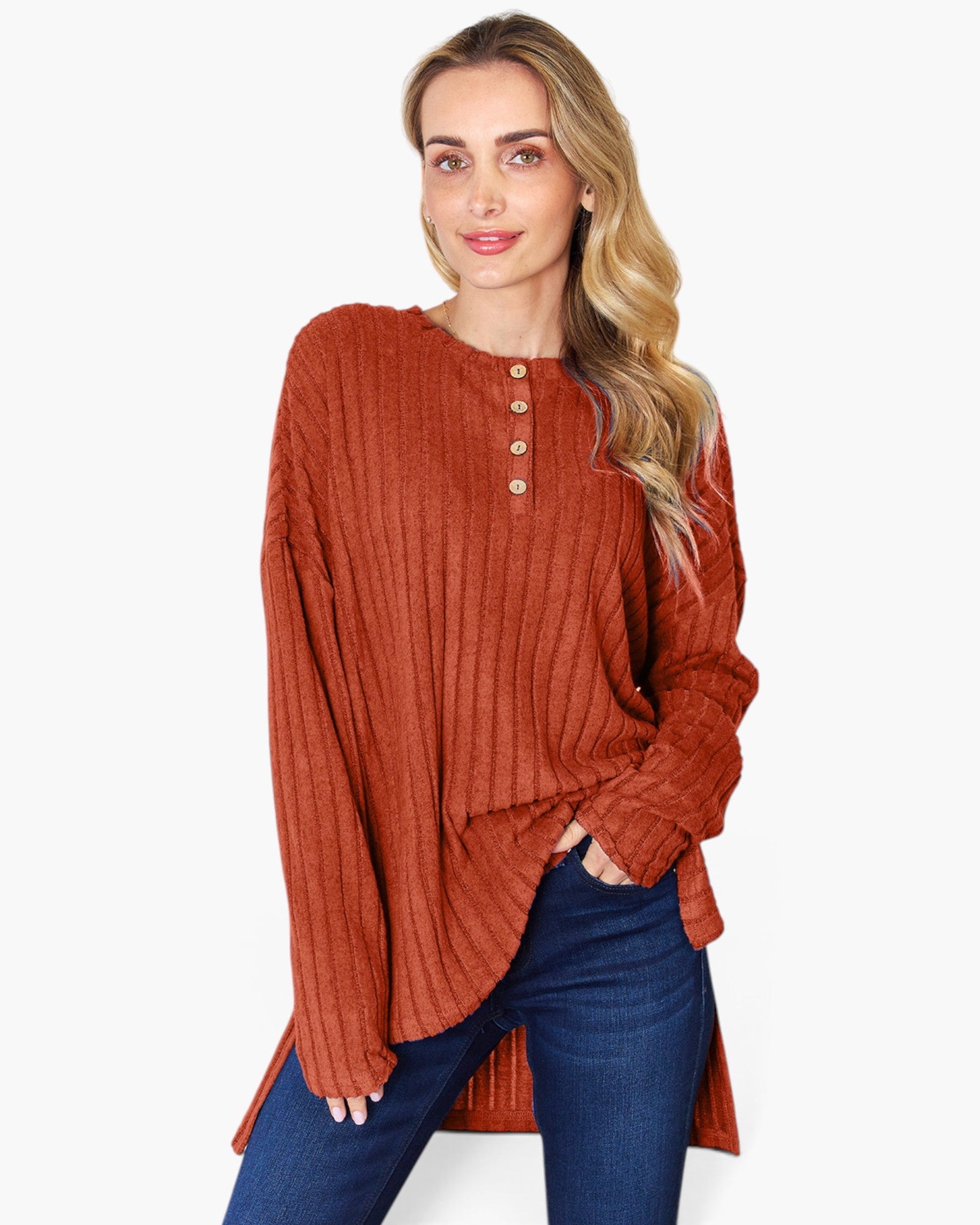 A woman wearing a rust-orange ribbed knit long-sleeve henley top with blue jeans, photographed against a plain light gray studio background.