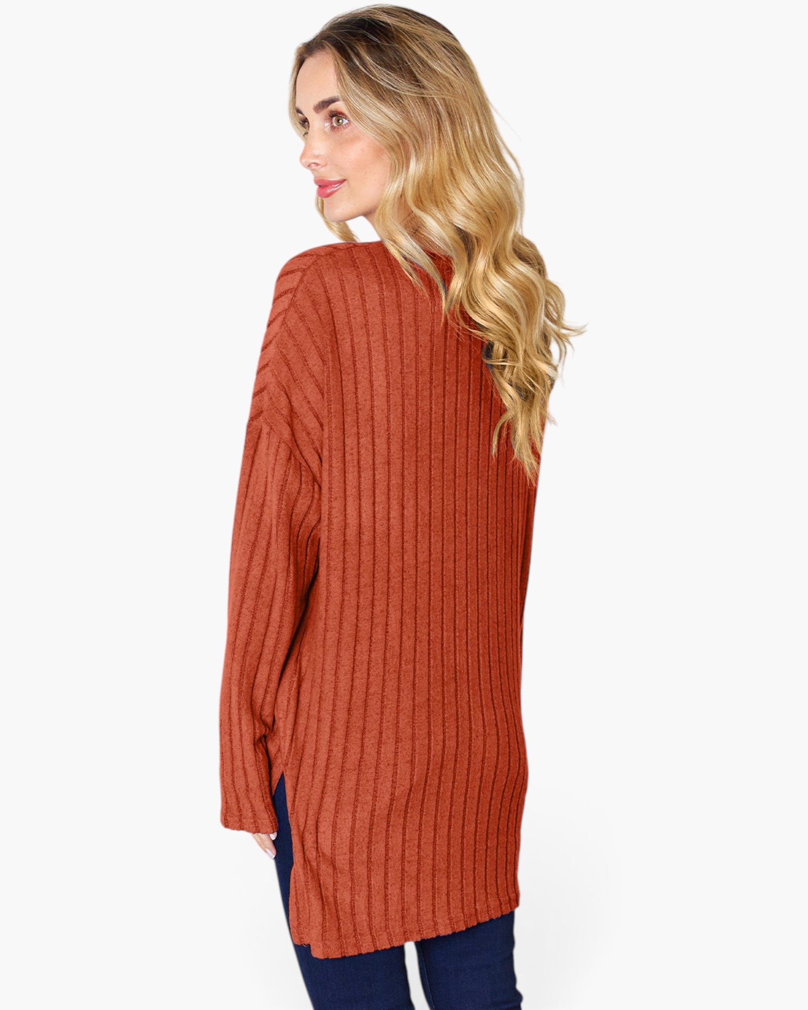 A woman with blonde hair is shown from a side-back angle wearing a rust-orange ribbed knit sweater and dark blue jeans against a plain white background.