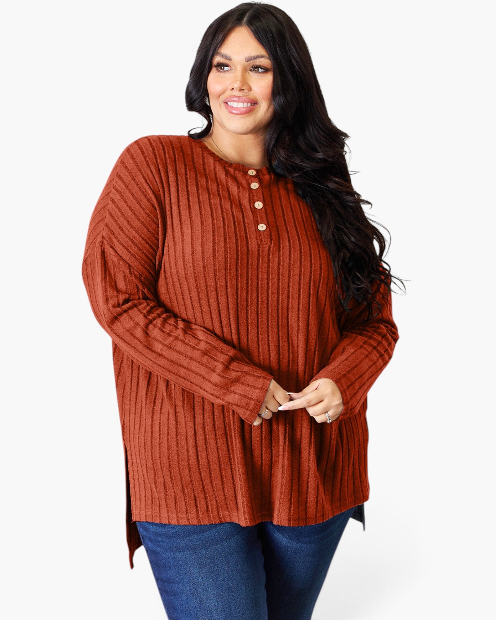A woman modeling a rust-orange ribbed knit long-sleeve henley top with three buttons at the collar, paired with blue jeans, against a plain white studio background.