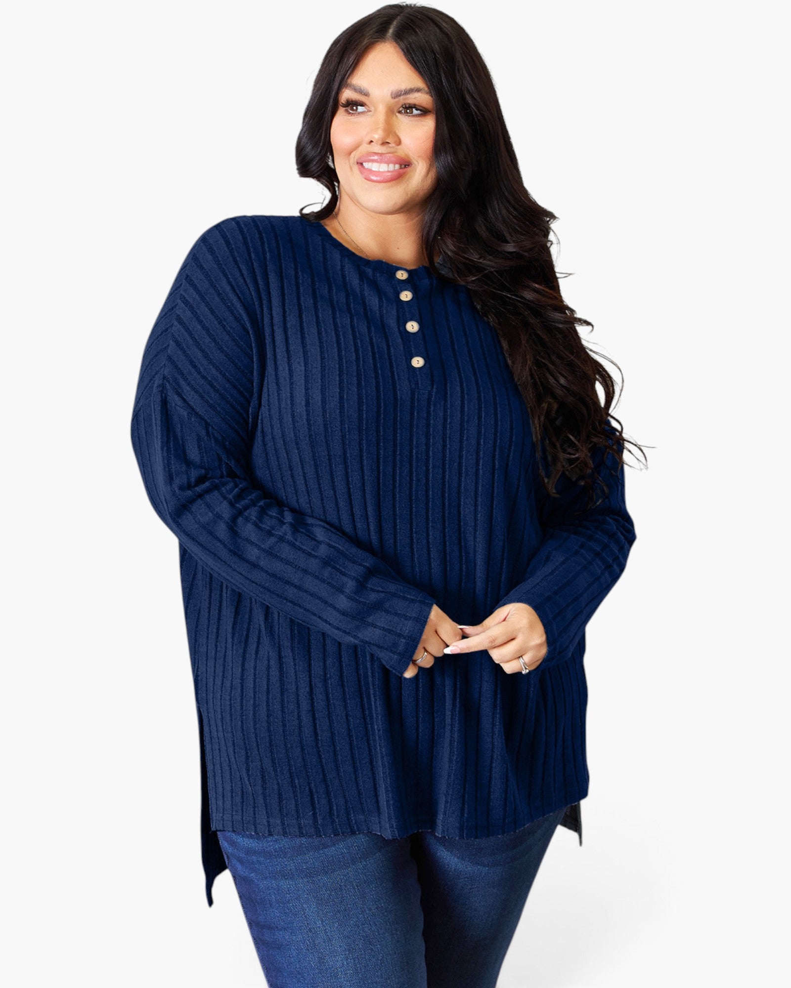 A woman modeling a navy blue ribbed knit long-sleeve tunic top with a three-button henley neckline, paired with blue jeans, against a plain white studio background.