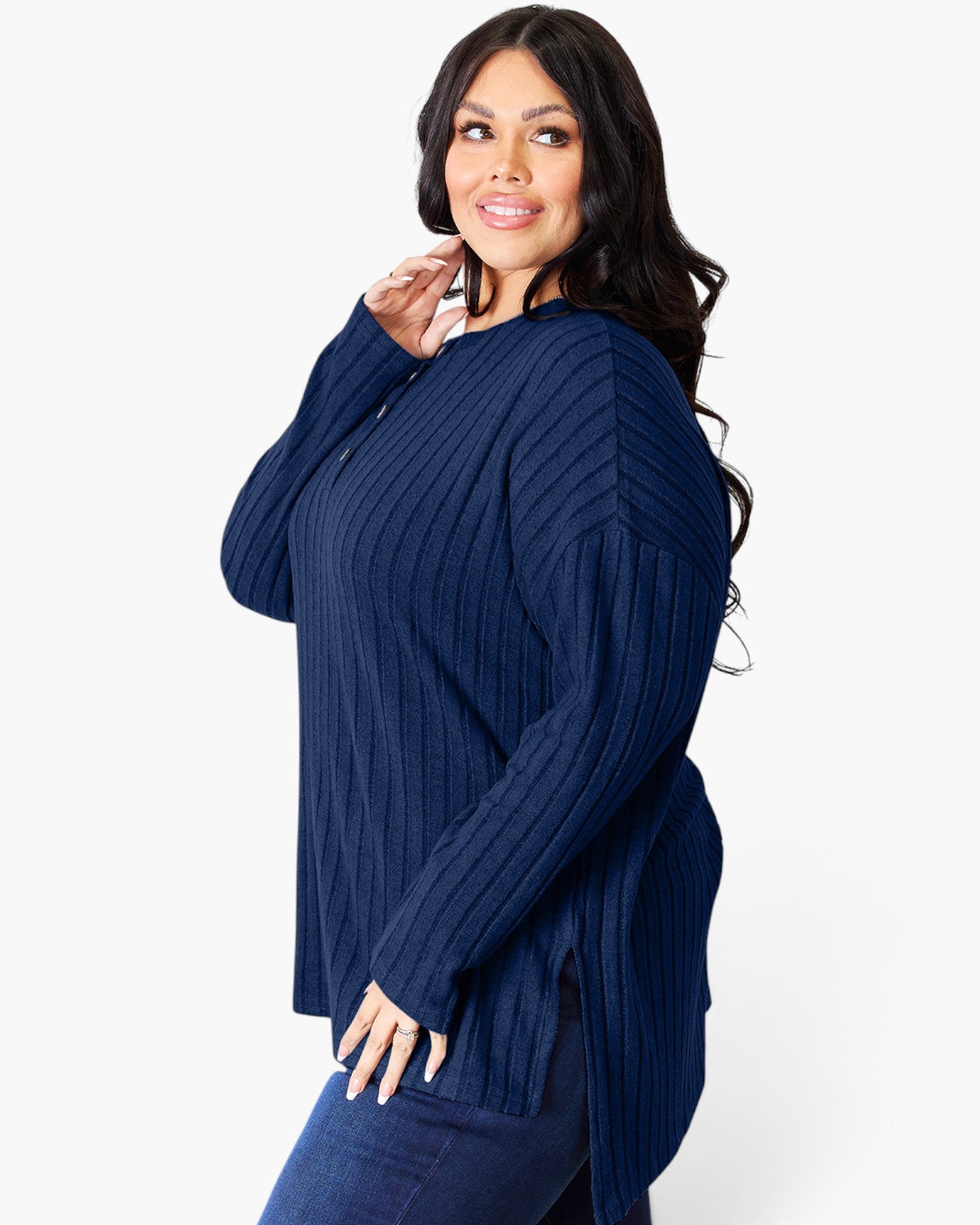 A woman modeling a navy blue ribbed knit long-sleeve top with a buttoned neckline, paired with dark blue jeans, against a plain white studio background.