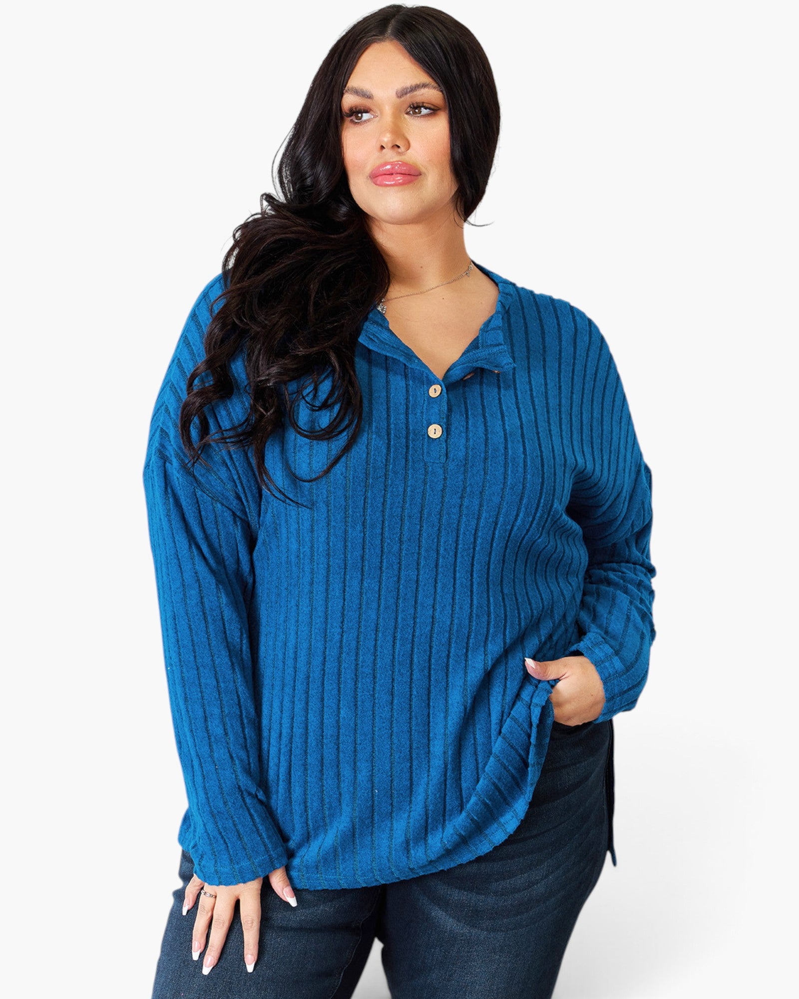 A woman modeling a blue ribbed knit long-sleeve polo shirt with a button placket, paired with dark jeans, against a plain white studio background.