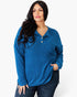 A woman modeling a blue ribbed knit long-sleeve polo shirt with a button placket, paired with dark jeans, against a plain white studio background.