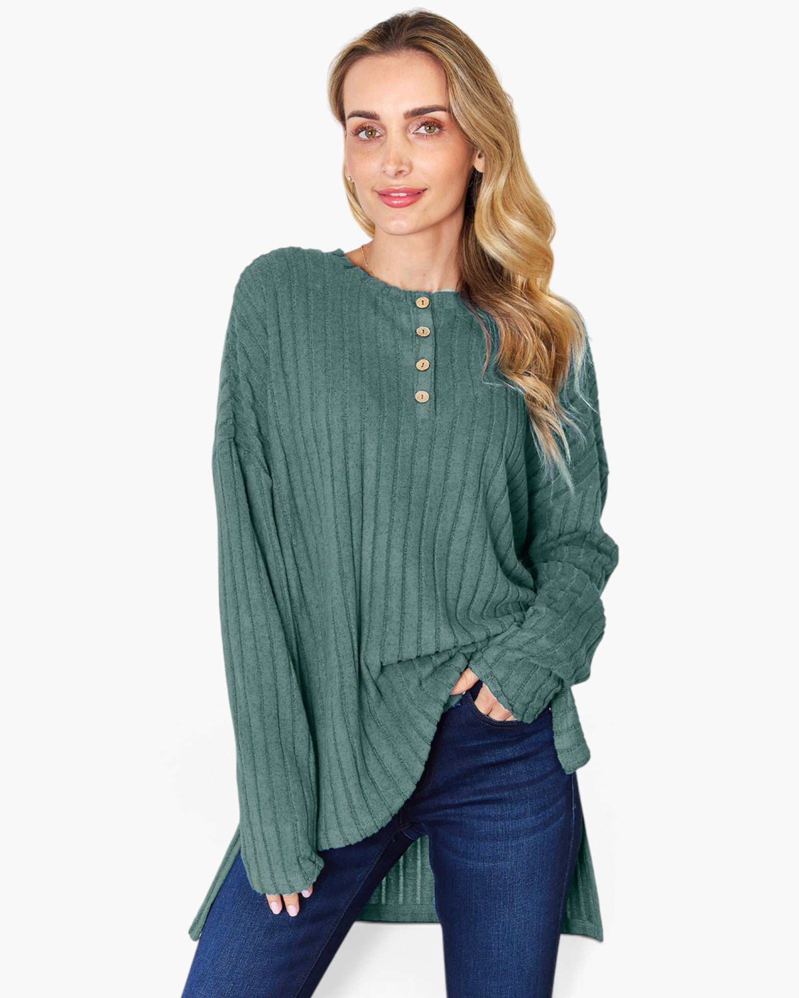A woman modeling a sage green ribbed knit long-sleeve top with a buttoned henley neckline, paired with dark blue jeans, against a plain white background.