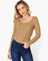 A woman wearing a tan ribbed long-sleeve scoop-neck top and dark blue jeans, standing against a plain white studio background.