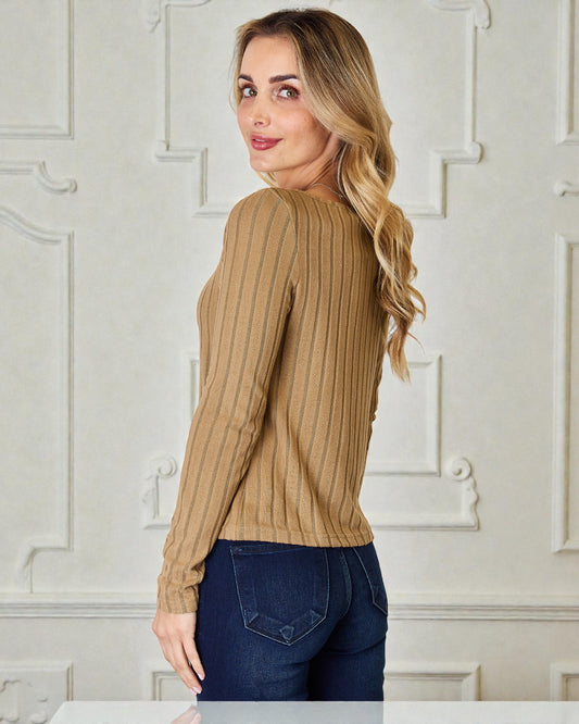 Woman wearing a brown ribbed sweater and blue jeans in a room with white paneled walls.