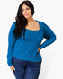 A woman modeling a bright blue ribbed knit sweater with a square neckline and long sleeves, paired with dark blue jeans, against a plain light gray background.