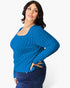 A woman modeling a bright blue ribbed knit long-sleeve top with a scoop neckline, paired with dark blue jeans, against a plain light gray background.