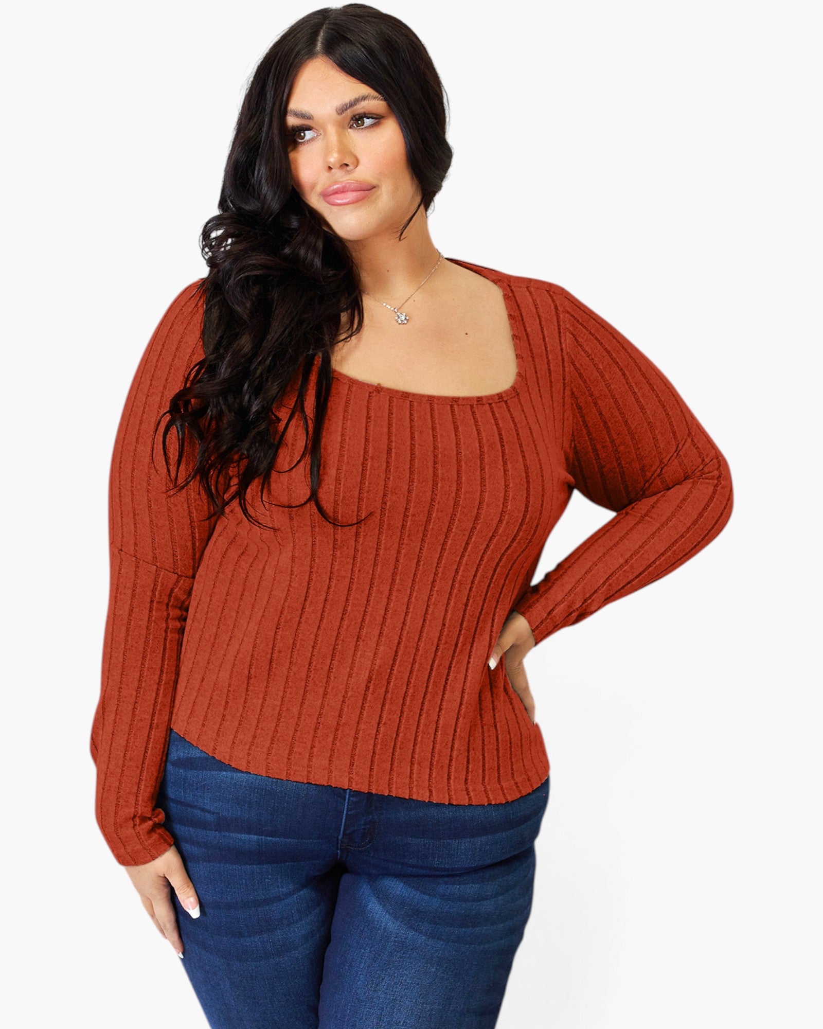 A woman modeling a rust-orange ribbed knit long-sleeve top with a square neckline, paired with dark blue jeans, against a plain white background.