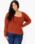 A woman modeling a rust-orange ribbed knit long-sleeve top with a square neckline, paired with dark blue jeans, against a plain white background.
