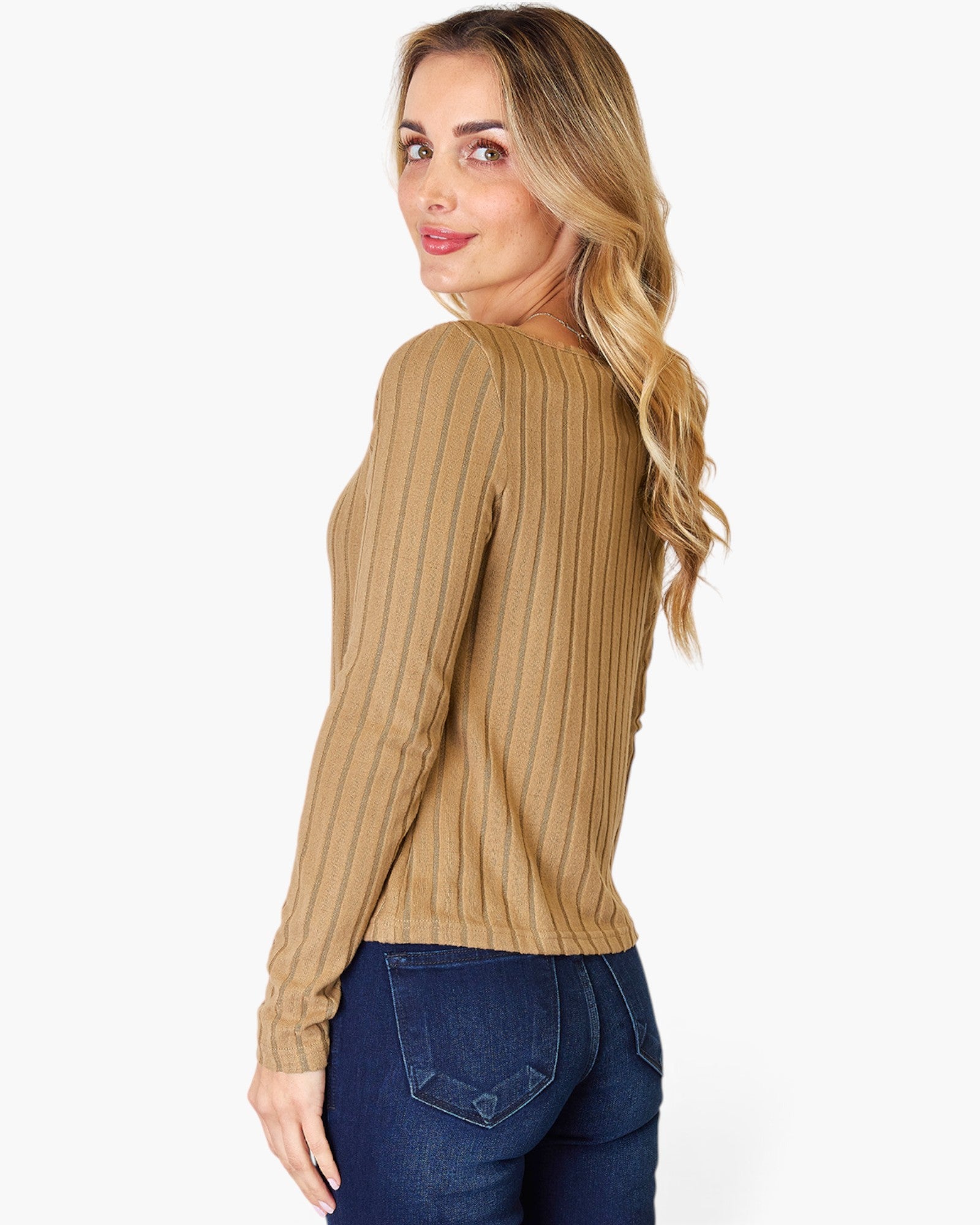 A woman wearing a tan ribbed long-sleeve knit top and dark blue jeans, shown from a side-back angle against a plain white studio background.