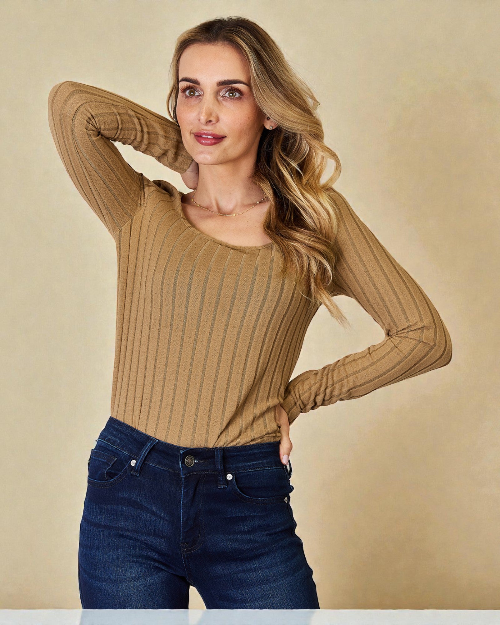 Woman wearing a brown ribbed sweater and blue jeans against a beige background