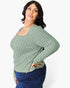 A woman modeling a sage green ribbed knit long-sleeve top with a scoop neckline, paired with dark blue jeans, against a plain white studio background.