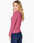 A woman with blonde hair is shown from a side-back angle wearing a pink ribbed knit sweater and dark blue jeans against a plain white background.