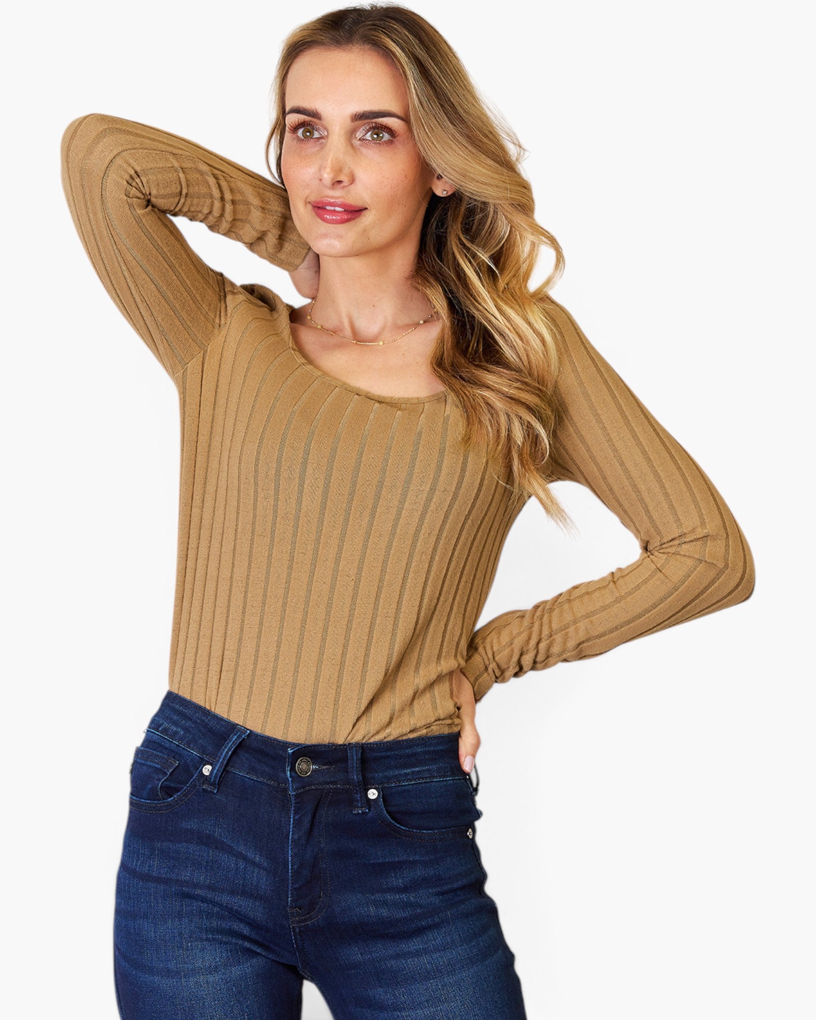 A woman modeling a tan ribbed long-sleeve scoop-neck top paired with dark blue jeans, set against a plain light gray background.