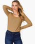 A woman modeling a tan ribbed long-sleeve scoop-neck top paired with dark blue jeans, set against a plain light gray background.