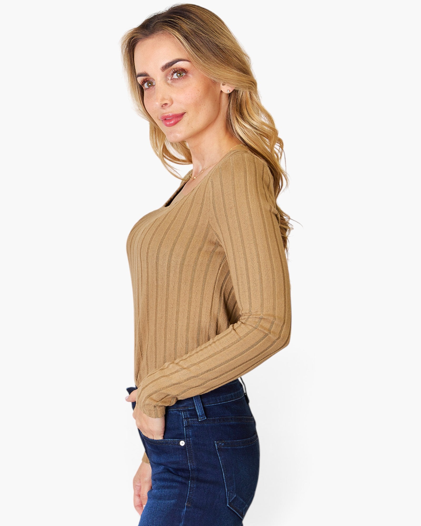 A woman wearing a tan ribbed long-sleeve top and dark blue jeans, shown from a side profile against a light gray background.