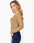 A woman wearing a tan ribbed long-sleeve top and dark blue jeans, shown from a side profile against a light gray background.