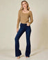 Woman wearing a brown ribbed sweater and dark blue flared jeans on a beige background