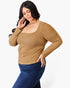 A woman modeling a tan ribbed long-sleeve scoop-neck top with structured shoulders, paired with dark blue jeans, against a plain white studio background.