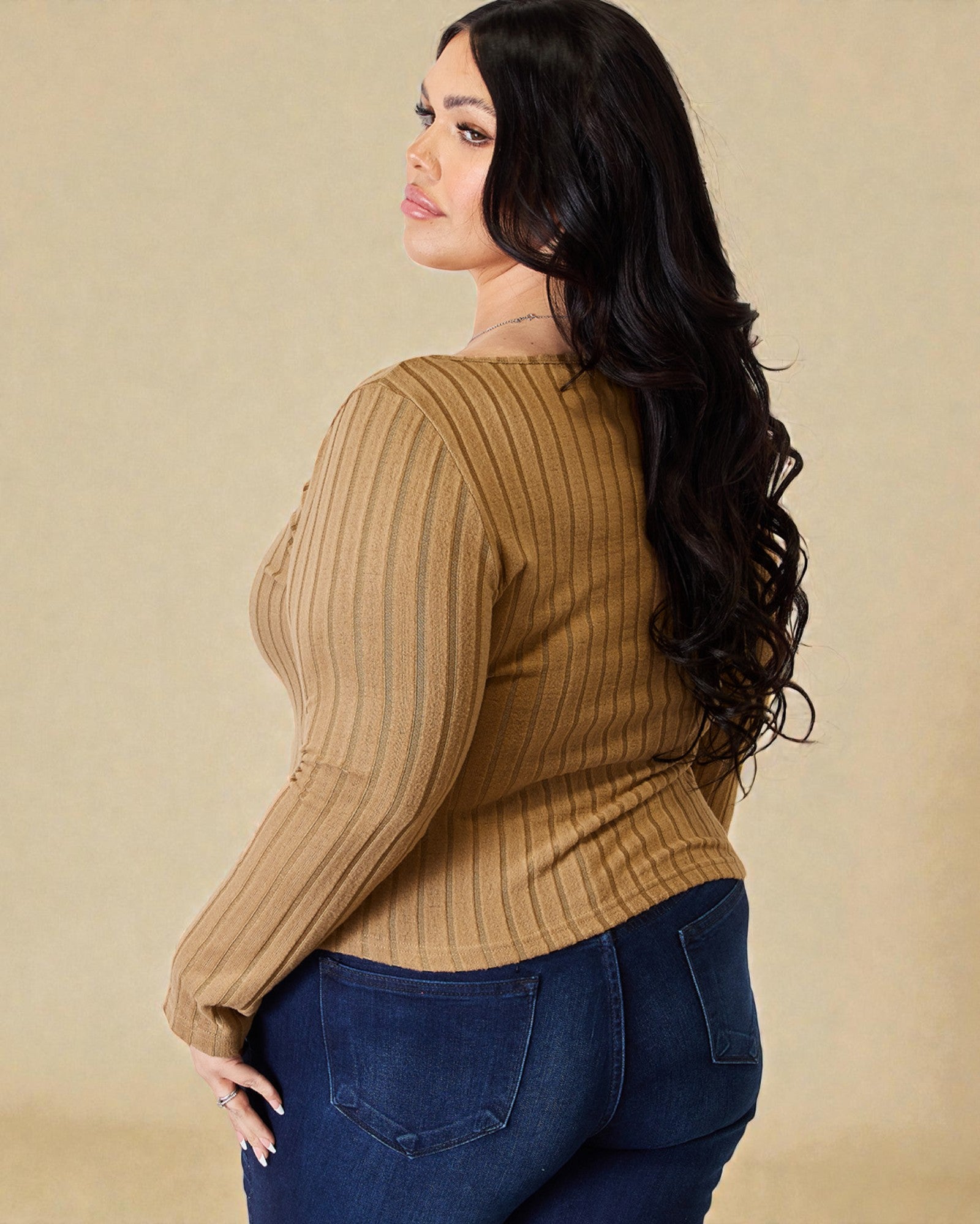 Woman wearing a brown ribbed sweater and blue jeans against a beige background
