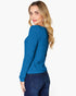 A woman with blonde hair is shown from a side-back angle wearing a blue ribbed knit sweater and dark blue jeans against a plain white background.