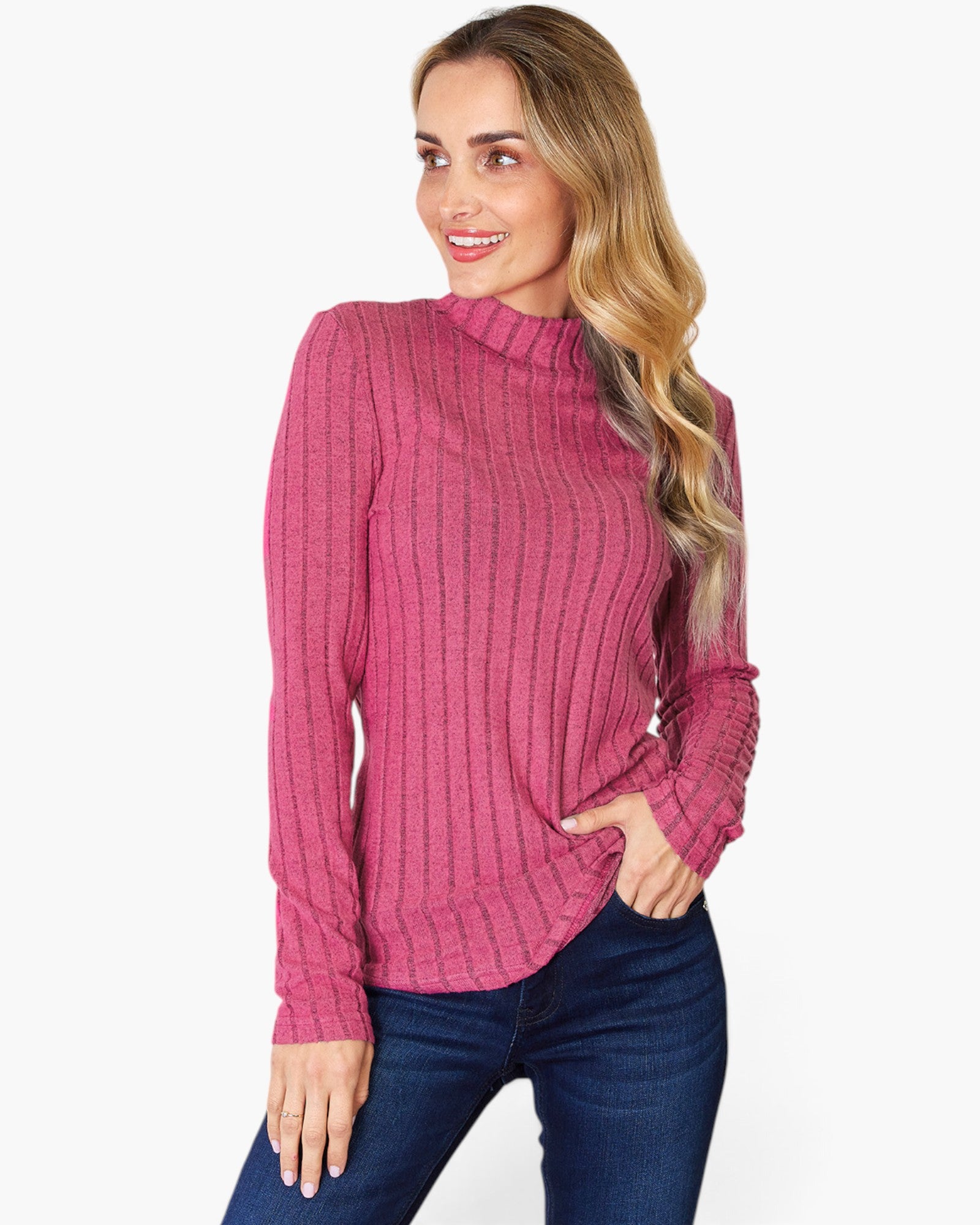 A woman wearing a pink ribbed mock neck long-sleeve top and dark blue jeans, standing against a plain white background.