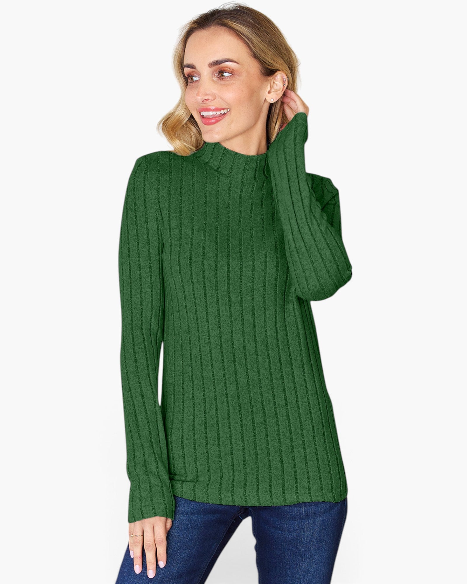 A woman wearing a green ribbed mock neck sweater and blue jeans, posing against a light gray background.