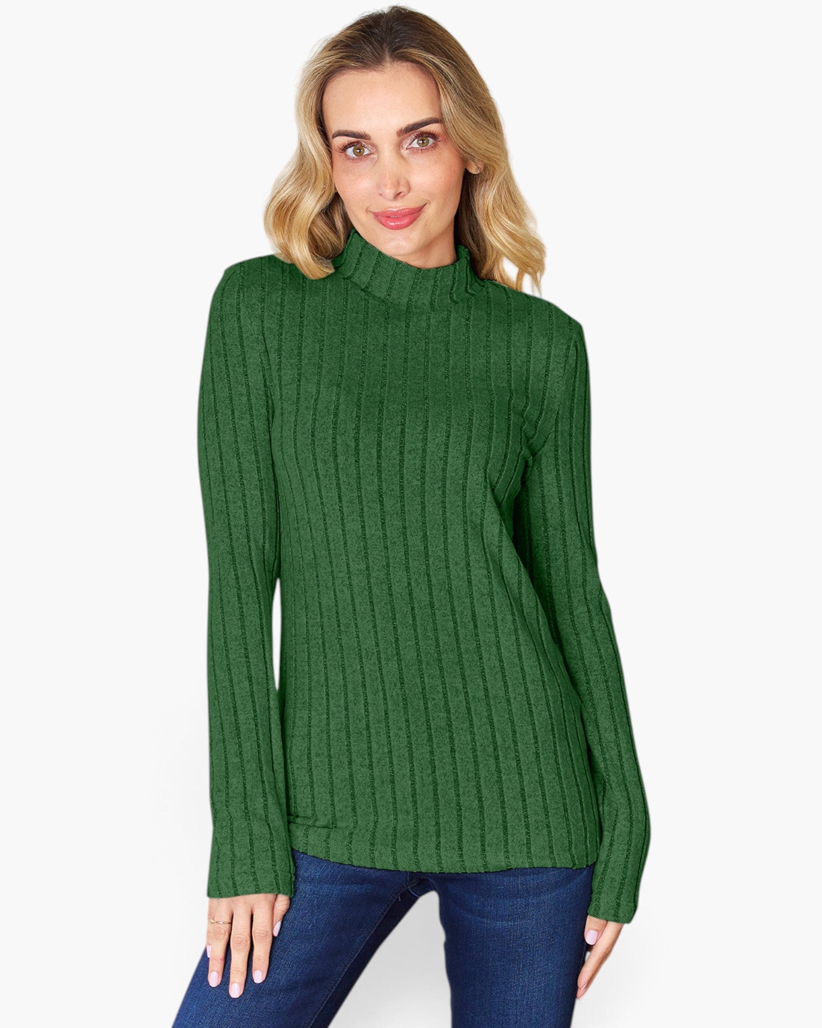A woman wearing a green ribbed mock neck sweater and blue jeans, standing against a plain white background.