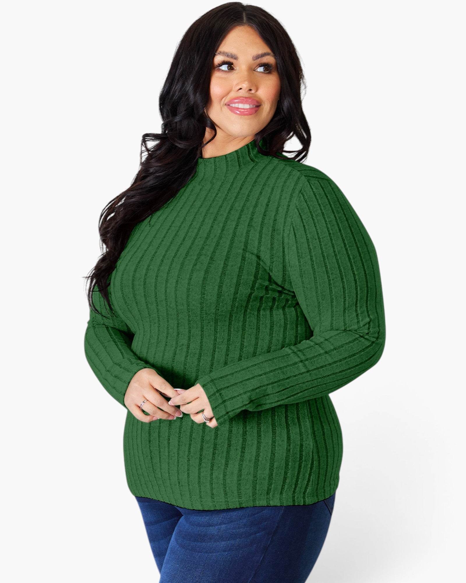 A woman modeling a green ribbed mock neck sweater with long sleeves, paired with blue jeans, against a plain white studio background.
