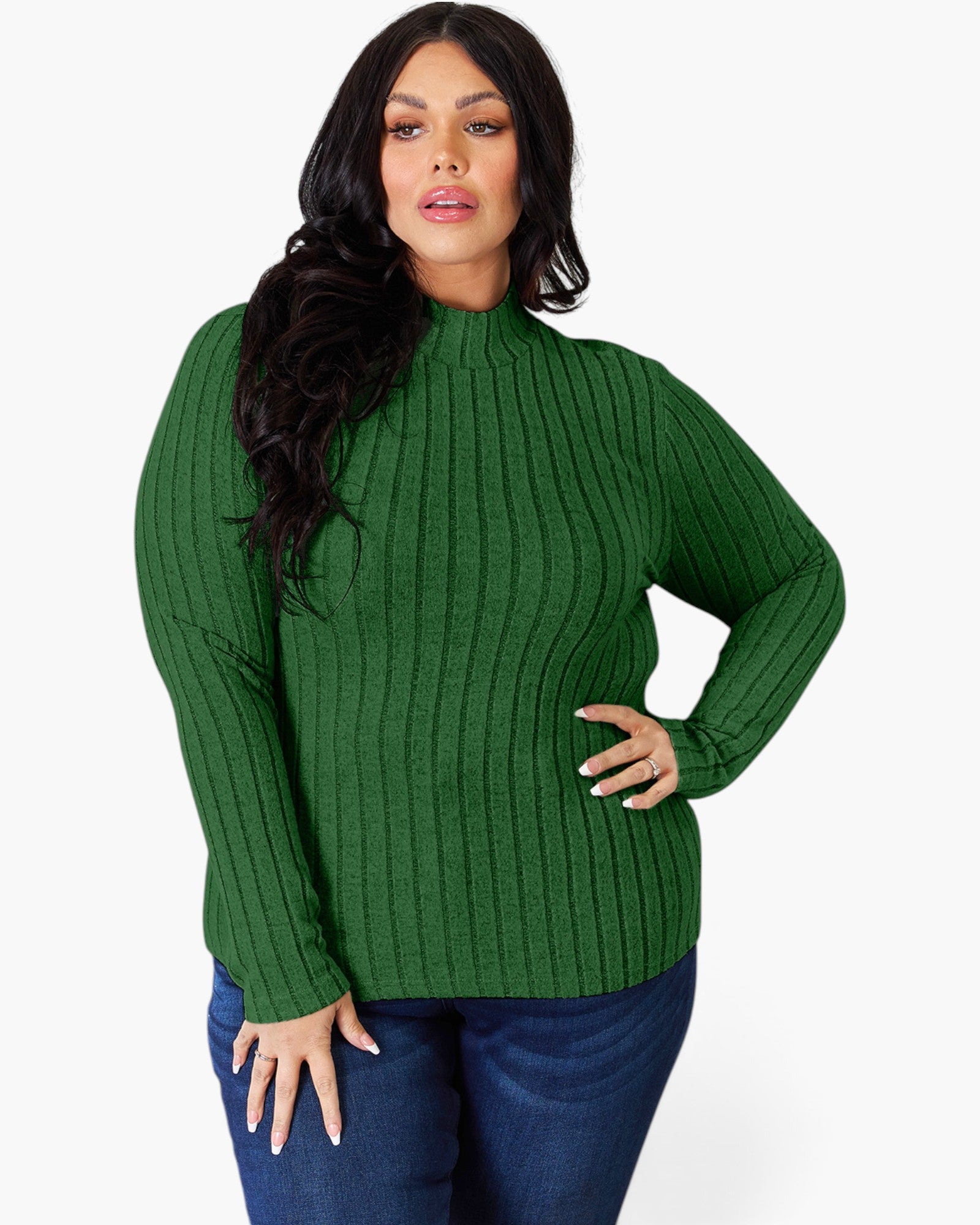 A woman modeling a green ribbed mock neck sweater with long sleeves, paired with blue jeans, against a plain light gray background.