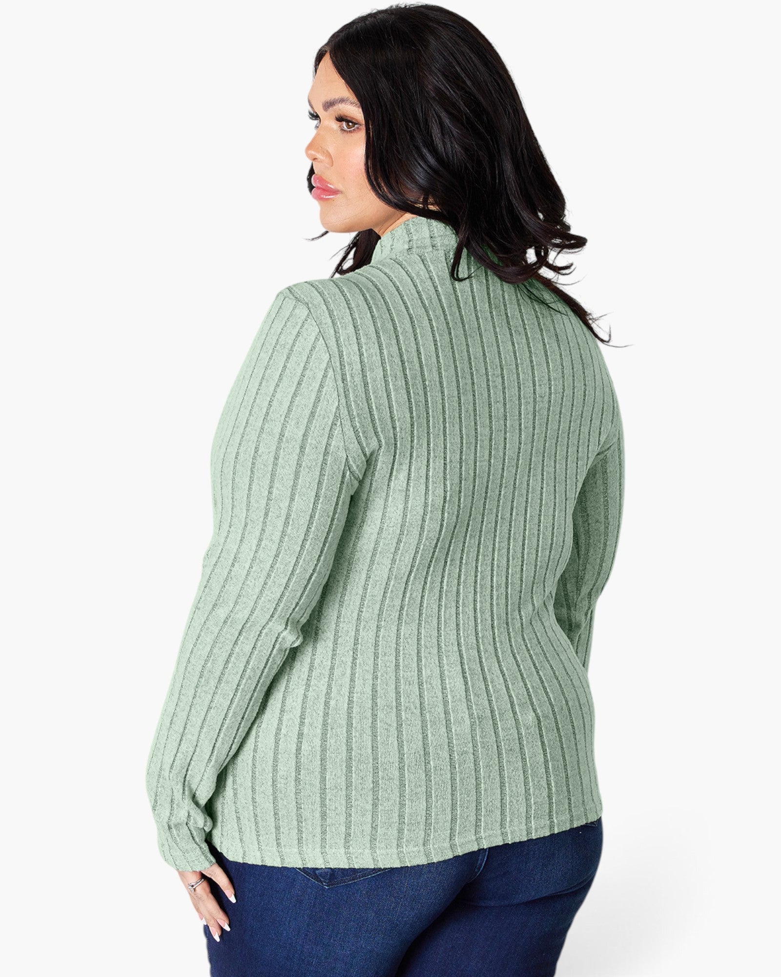 A woman shown from the back wearing a sage green ribbed knit sweater and dark blue jeans against a plain white studio background.