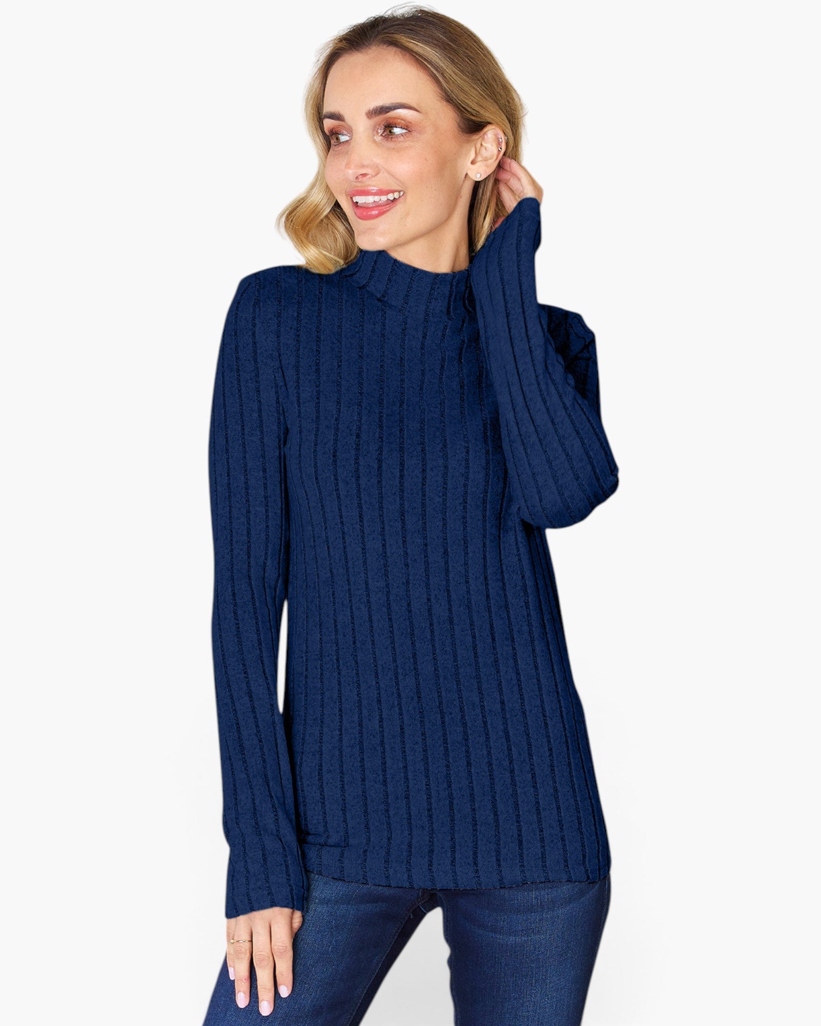 A woman wearing a navy blue ribbed mock neck sweater and dark blue jeans, posing against a light gray studio background.
