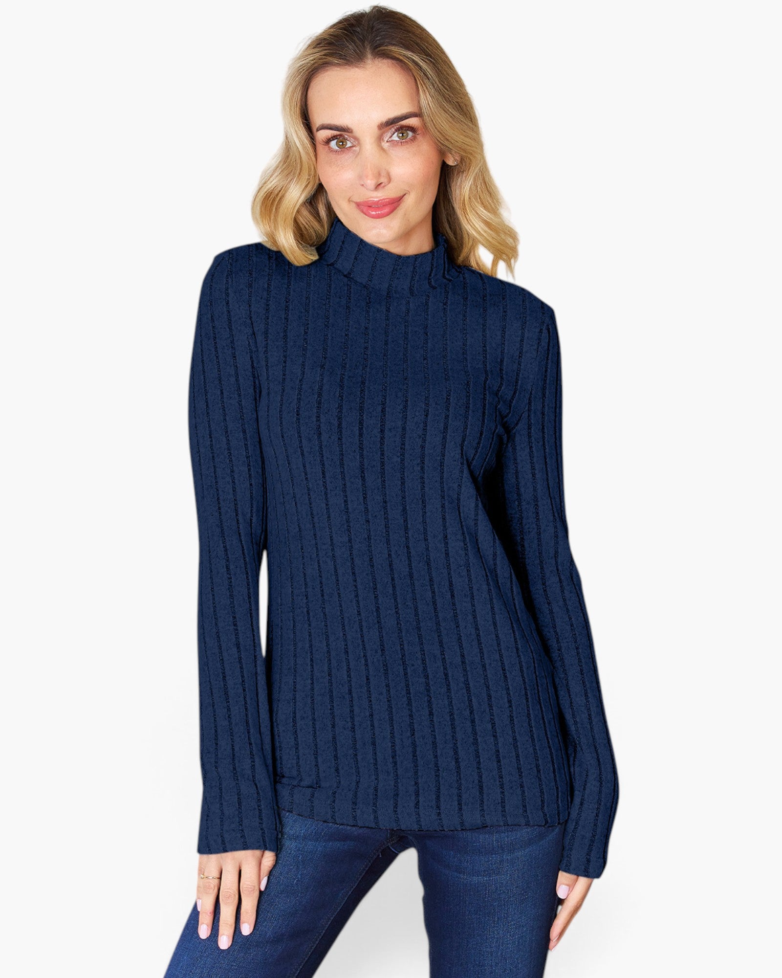 A woman wearing a navy blue ribbed mock neck sweater and dark blue jeans, standing against a plain white studio background.