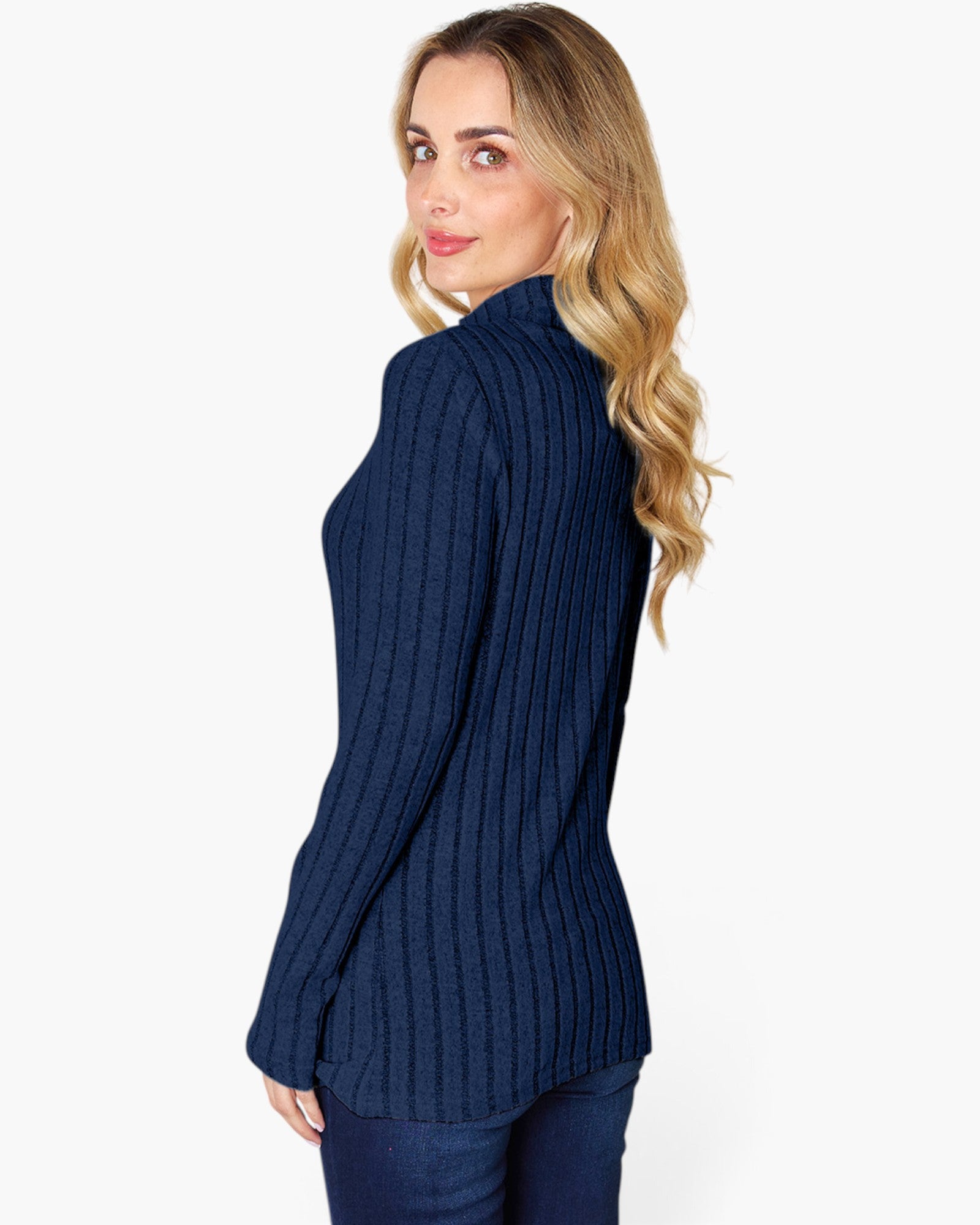 A woman with blonde wavy hair is shown from the side/back wearing a navy blue ribbed knit mock neck sweater and dark blue jeans against a plain white studio background.