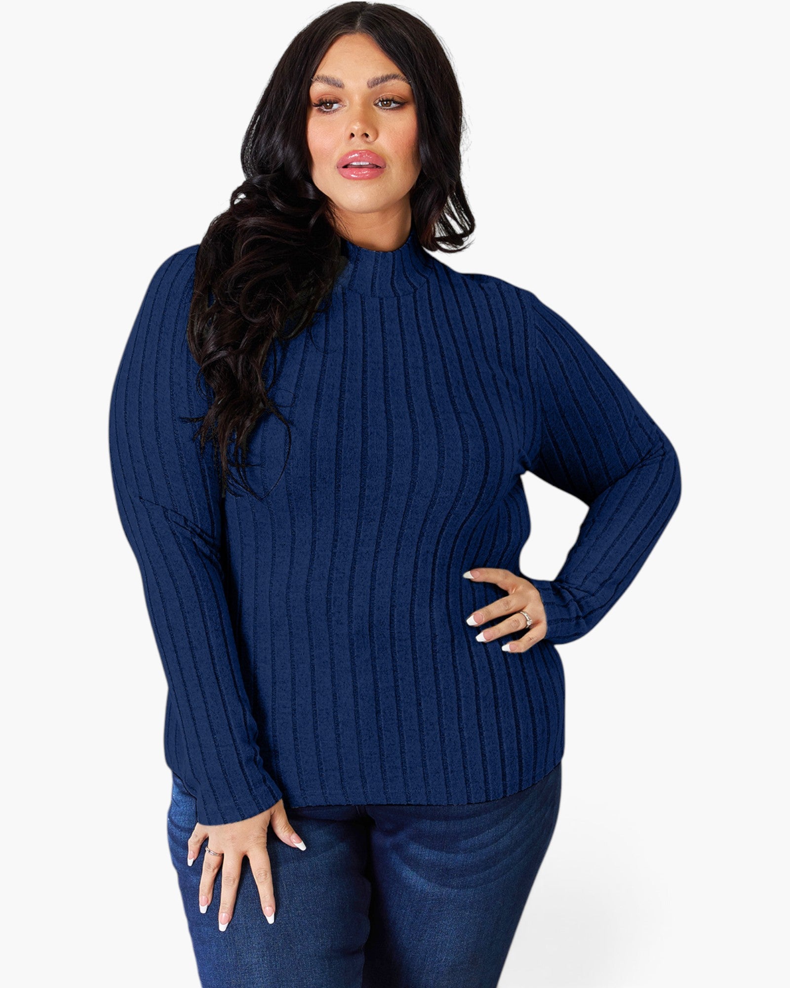 A woman modeling a navy blue ribbed knit mock neck sweater with long sleeves, paired with dark blue jeans, against a plain light gray background.