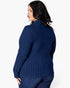 A woman shown from the back wearing a navy blue ribbed knit sweater and dark blue jeans against a plain white studio background.