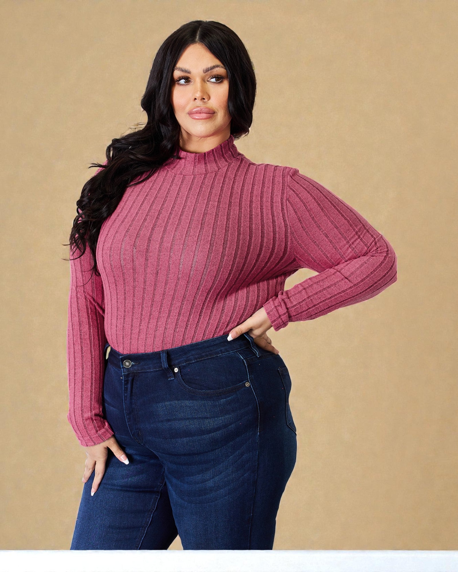 Woman wearing a ribbed pink sweater and blue jeans against a beige background