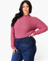 A woman modeling a long-sleeve ribbed mock neck top in dusty rose pink, paired with dark blue jeans, against a plain white studio background.