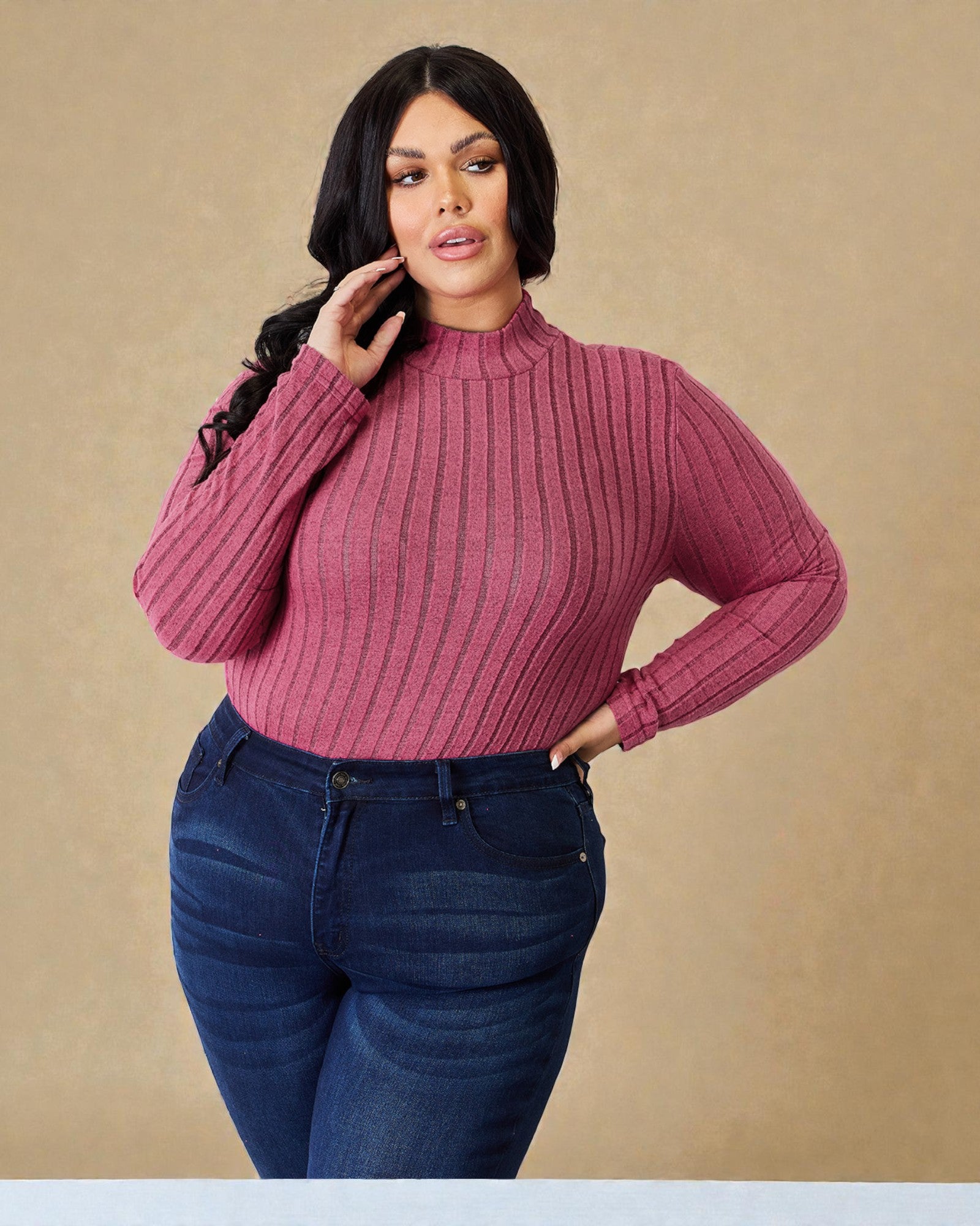 Woman wearing a pink ribbed sweater and blue jeans against a beige background