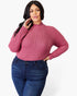 A woman modeling a ribbed long-sleeve mock neck sweater in dusty rose pink, paired with dark blue jeans, against a plain white studio background.