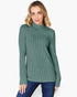 A woman wearing a ribbed knit mock neck sweater in a dusty sage green color, paired with dark blue jeans, against a plain white background.