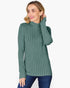 A woman wearing a ribbed knit mock neck sweater in a dusty sage green color, paired with dark blue jeans, against a plain white background.
