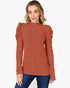 A woman wearing a rust-orange ribbed knit mock-neck sweater with puffed sleeves, paired with blue jeans, against a plain white background.