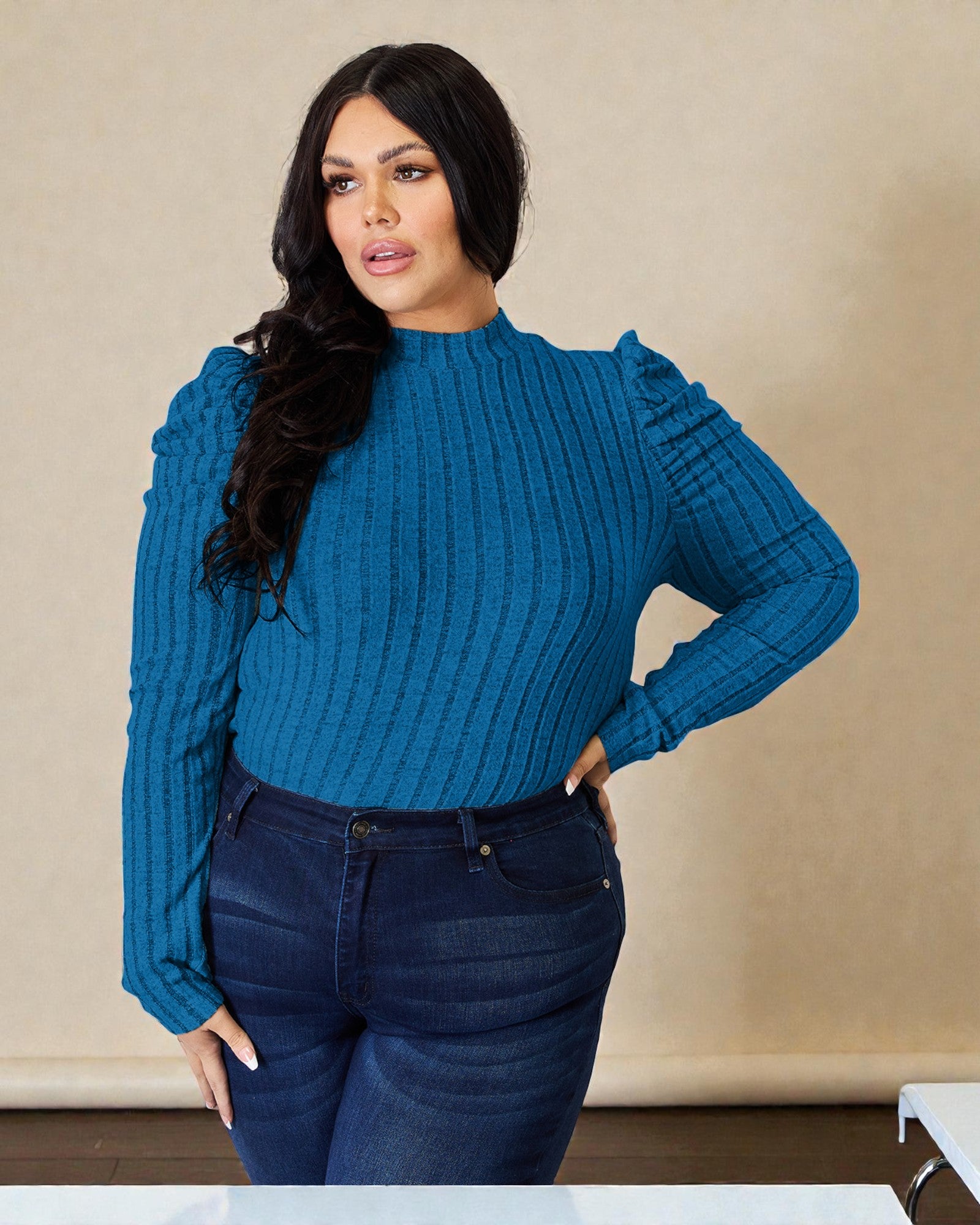 Woman wearing a blue ribbed sweater and dark jeans against a beige background